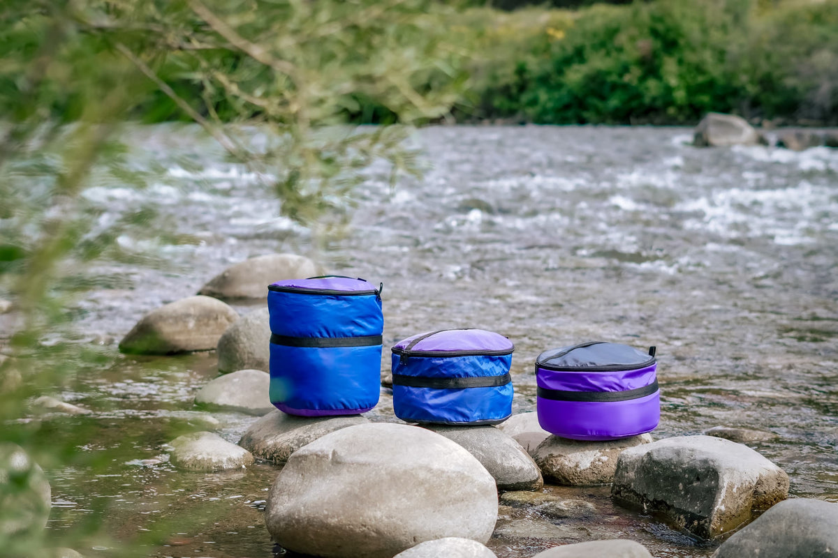 Three Ruby Moons packing rounds in blue and purple, set on rocks along a river