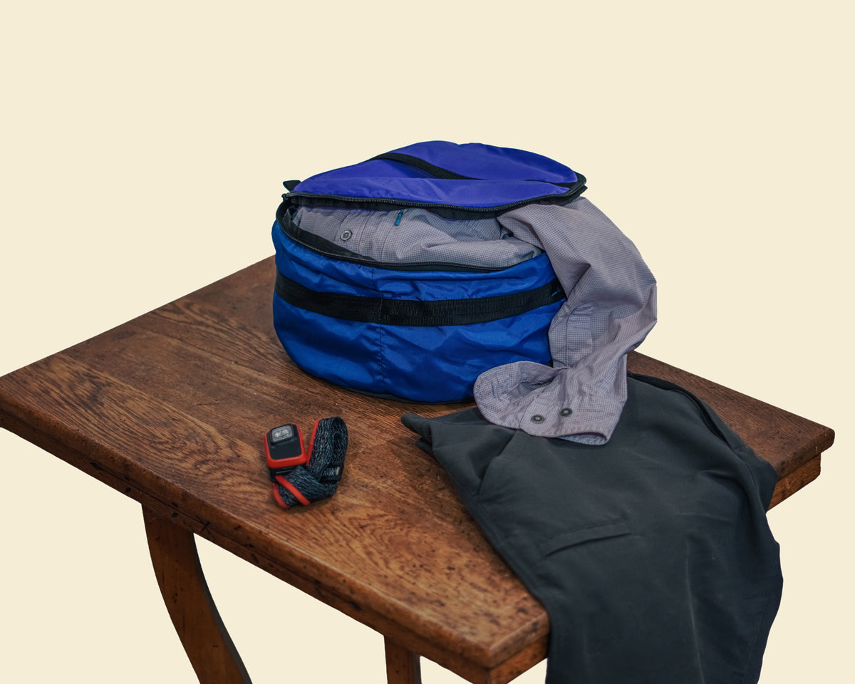 Ruby Moons packing round dry bag with a shirt hanging out and shorts and a headlamp laid beside it, shown on a light beige background