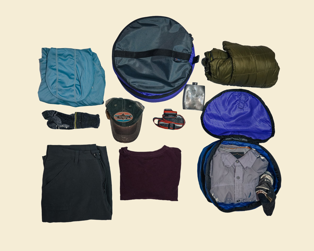 Two Ruby Moons packing round dry bags surrounded by folded clothing and miscellaneous gear, shown on a light beige background