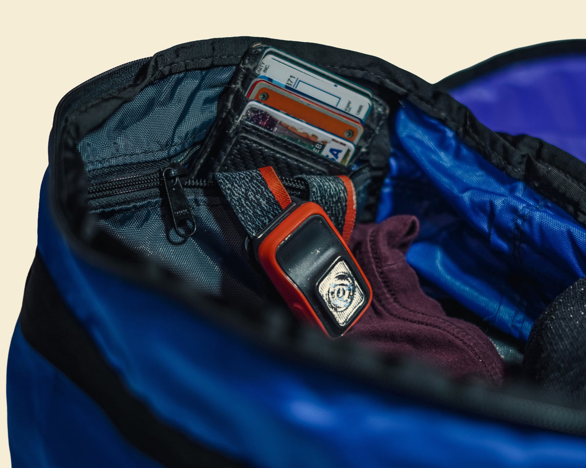 Close-up of a Ruby Moons packing round's Eddy Pocket partially closed, with a headlamp and wallet tucked inside, shown on a light beige background