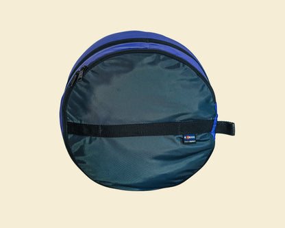 A round, zippered hard case in dark teal-blue nylon with a bright blue top rim and a black horizontal compression strap, shown against a solid light beige background.