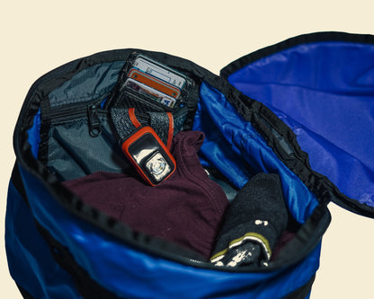 Close-up of a Ruby Moons packing round's Eddy Pocket partially closed, with a headlamp and wallet tucked inside, shown on a light beige background